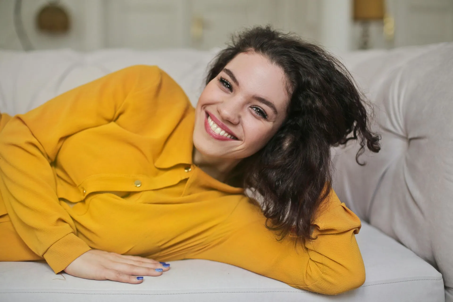 A woman in yellow shirt laying on couch.