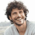Smiling man with curly hair outdoors.